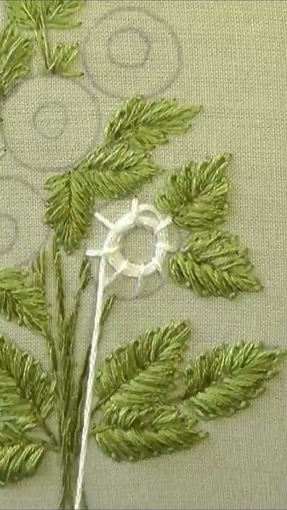 a close up of a piece of cloth with green leaves on it and thread in the middle