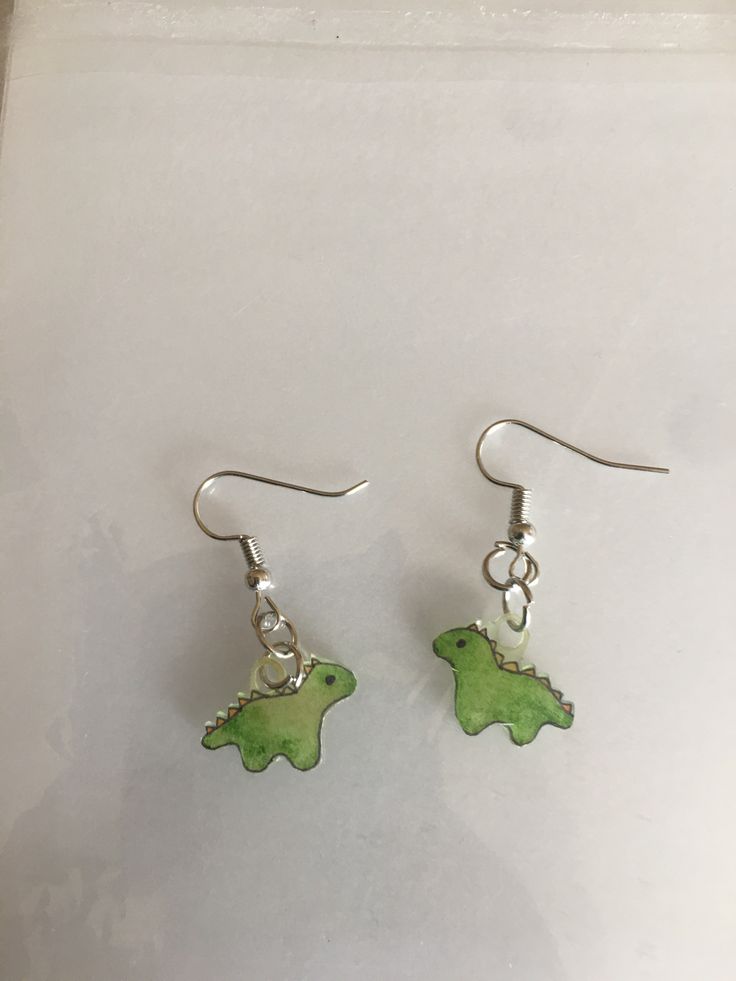 a pair of green dinosaur earrings sitting on top of a white table next to each other