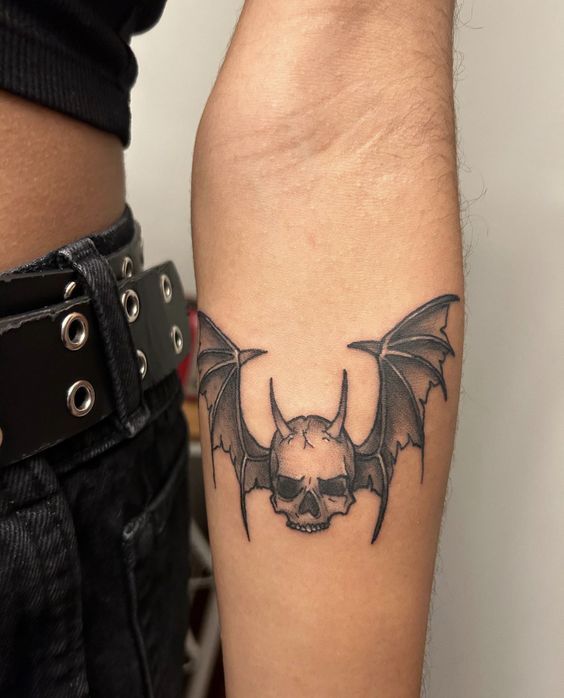 a black and white photo of a bat tattoo on someone's left arm with a skull in the middle