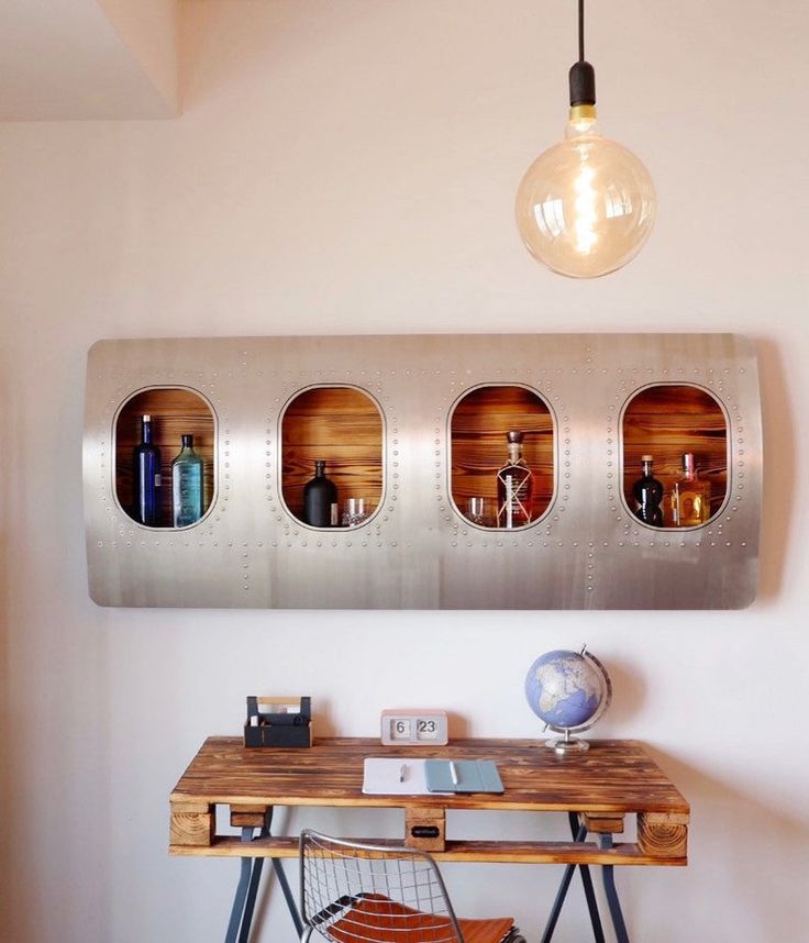 a wooden table topped with a metal wall mounted mirror next to a lamp and desk