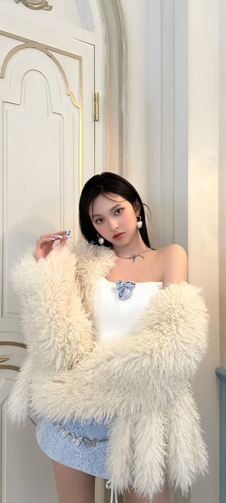 a woman is posing in front of a door wearing a white top and furry coat