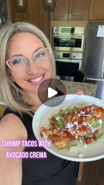 a woman holding a plate with shrimp tacos and avocado crema