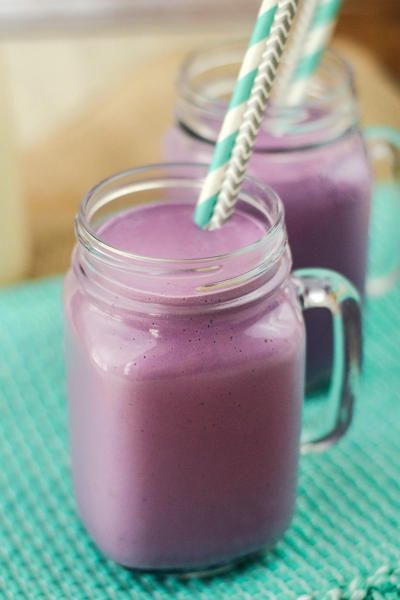 two mason jars filled with purple smoothie on a green place mat and one has a straw in it