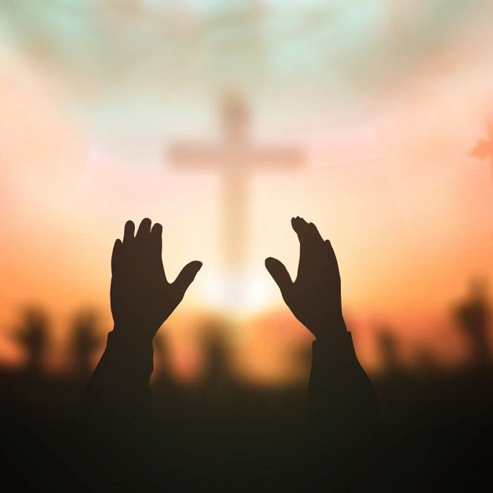 two hands raised up in front of a cross with the sun setting behind them and silhouettes of people raising their hands