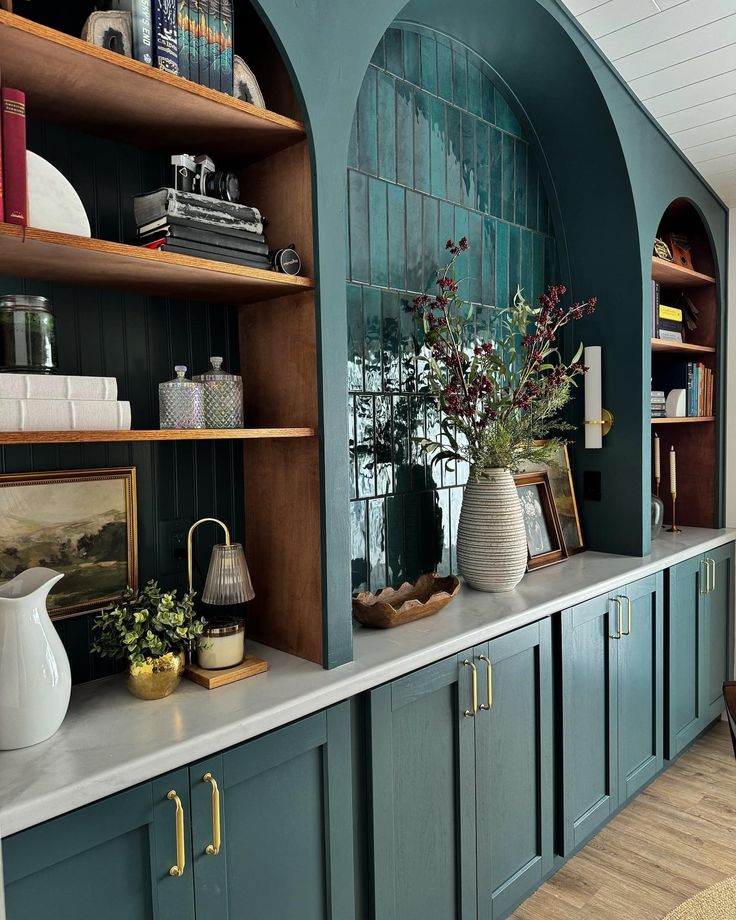 a kitchen with blue cabinets and white vases on the counter top, along with bookshelves