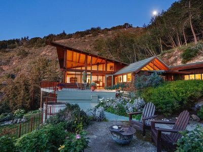 a house on the side of a hill with chairs and tables in front of it