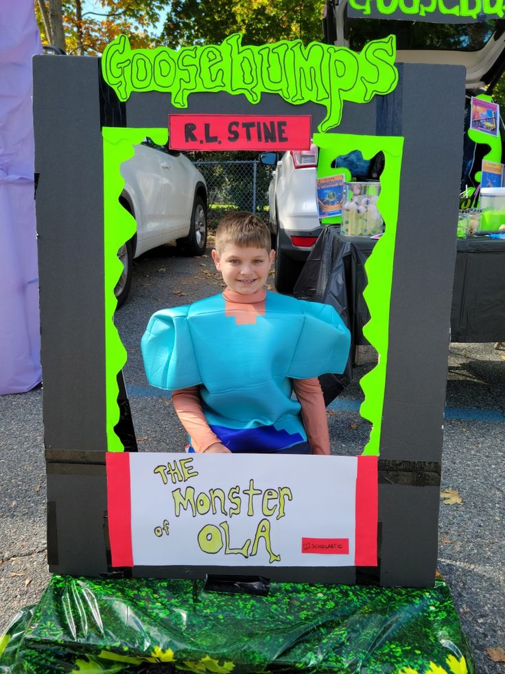 a young boy dressed as a monster in front of a costume contest sign for the monsters of olia