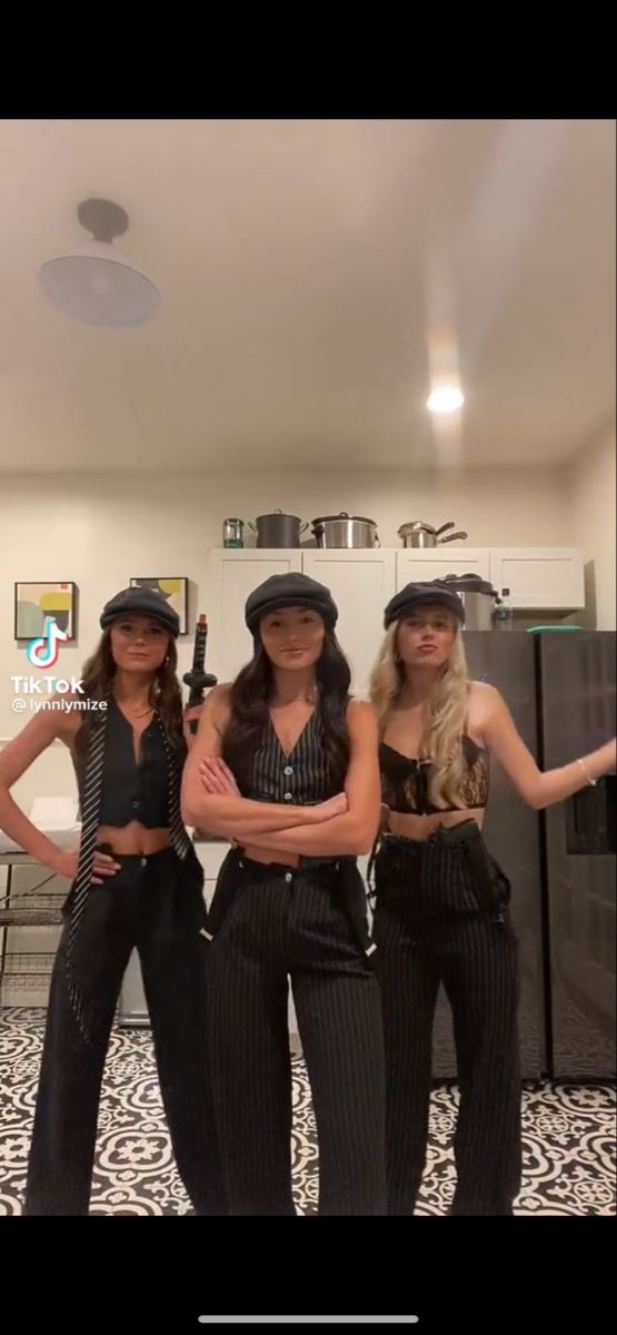 three women standing in front of a mirror wearing black outfits and hats with their arms crossed