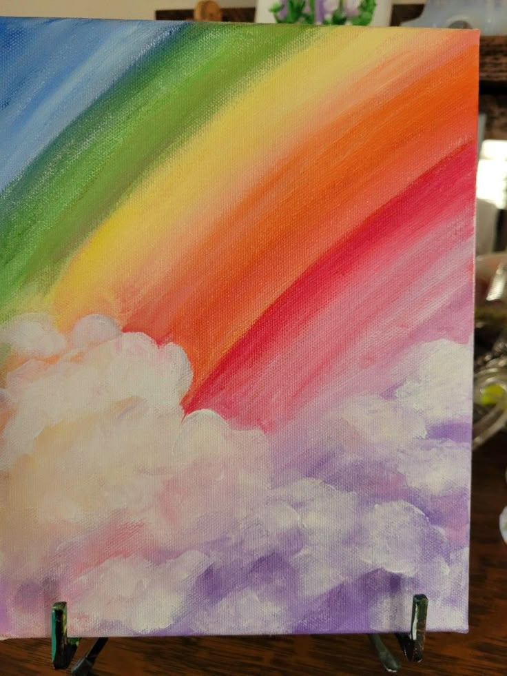 a painting of a rainbow in the sky on a easel with two green pegs