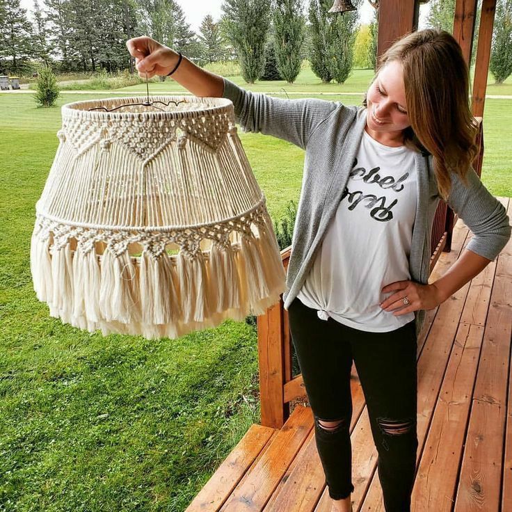 a woman standing on a porch holding up a lamp shade that is hanging from the ceiling