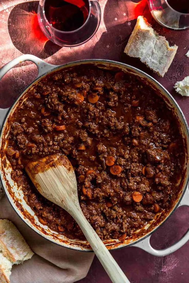 a pot filled with chili and bread next to two glasses of wine on a table