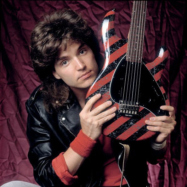 a young man holding an electric guitar in front of a red and black background,