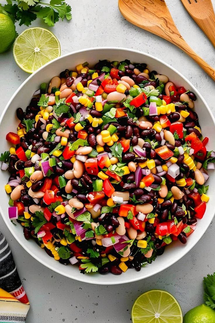 a white bowl filled with black beans and veggies next to lime wedges