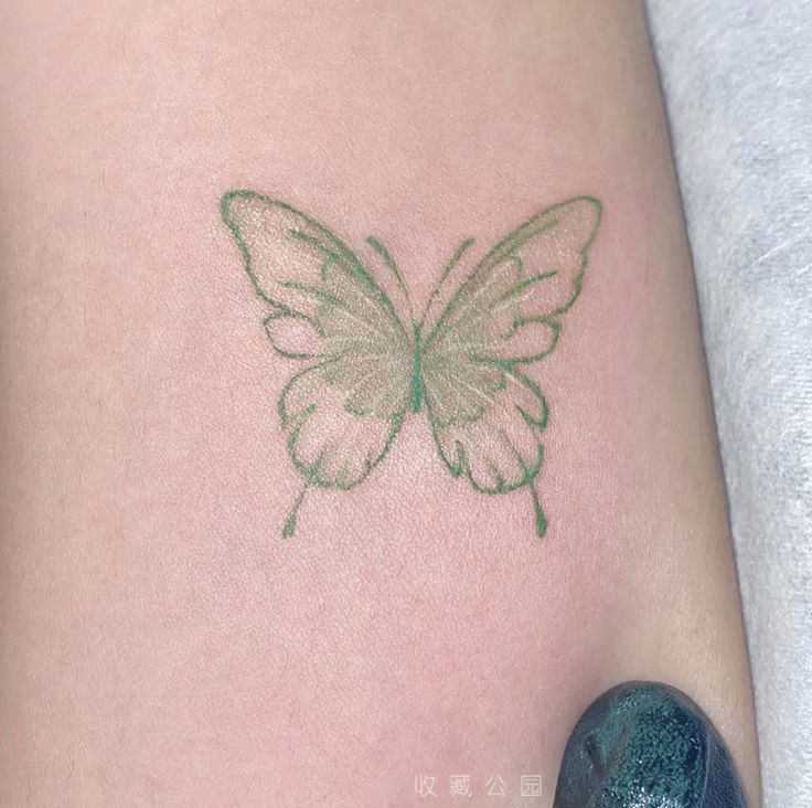 a small green butterfly tattoo on the back of a woman's arm and leg