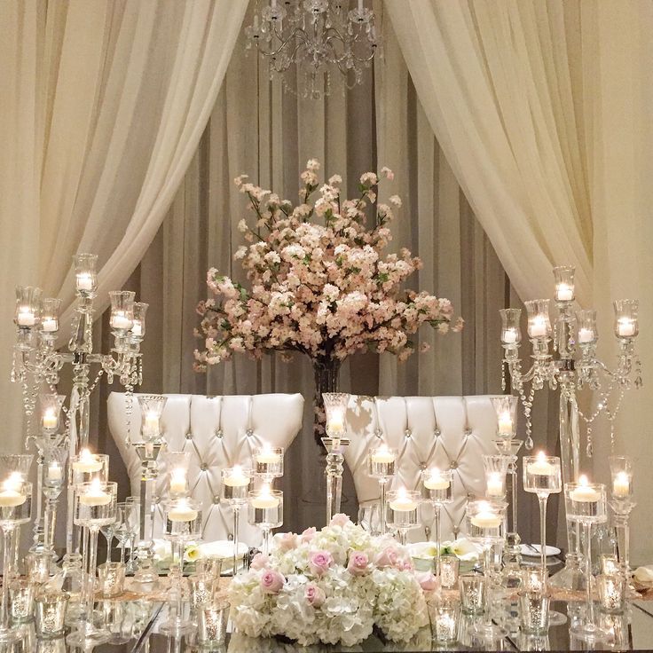 a table topped with lots of candles and vases filled with flowers next to a chandelier