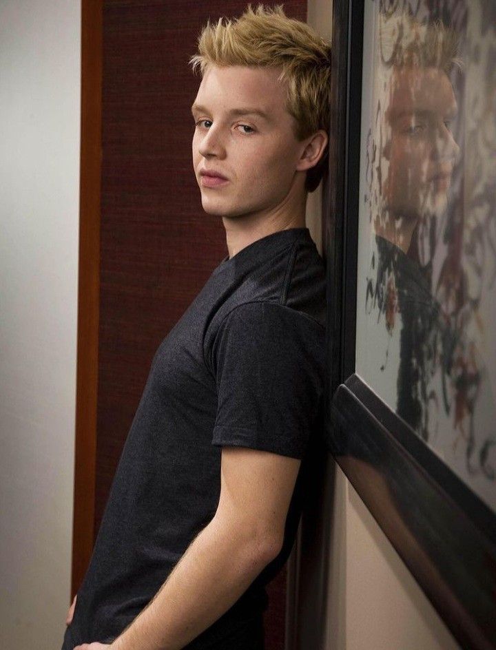 a young man leaning against a wall with his hand on his hip