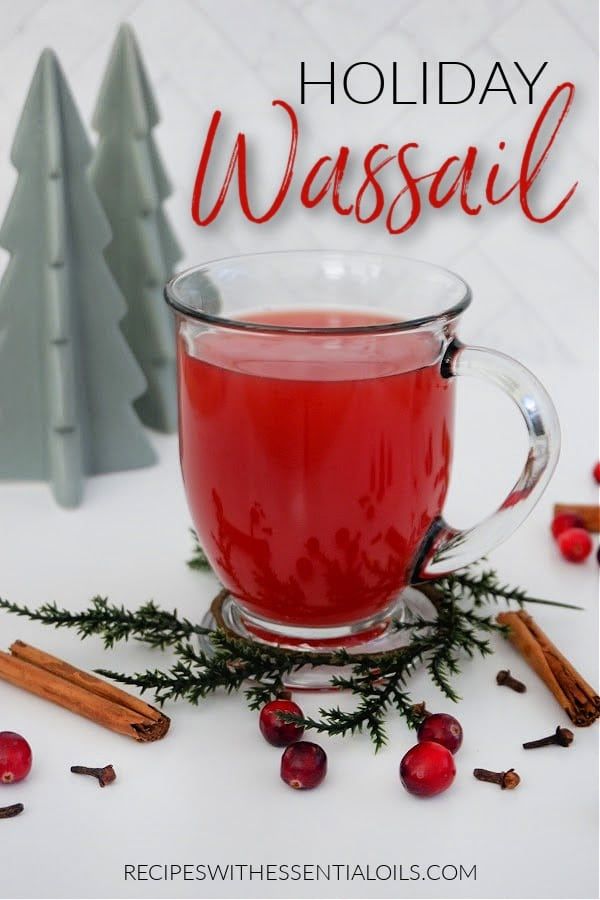 a glass mug filled with red liquid next to christmas trees and cinnamons on a white table