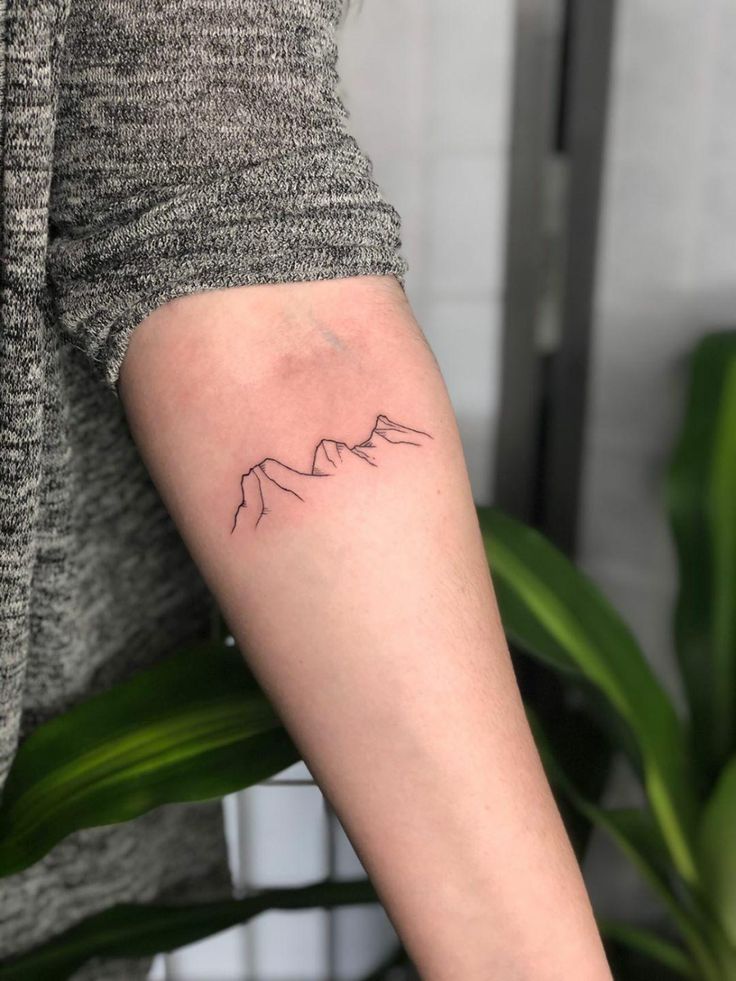 a woman's arm with a small mountain tattoo on the left side of her arm