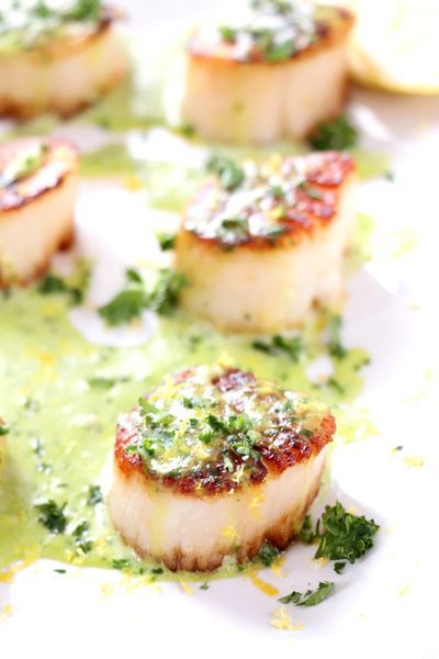 some scallops are sitting on a plate with sauce and garnishes