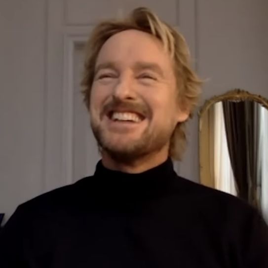 a man smiling and wearing a black turtle neck sweater in front of a gold mirror