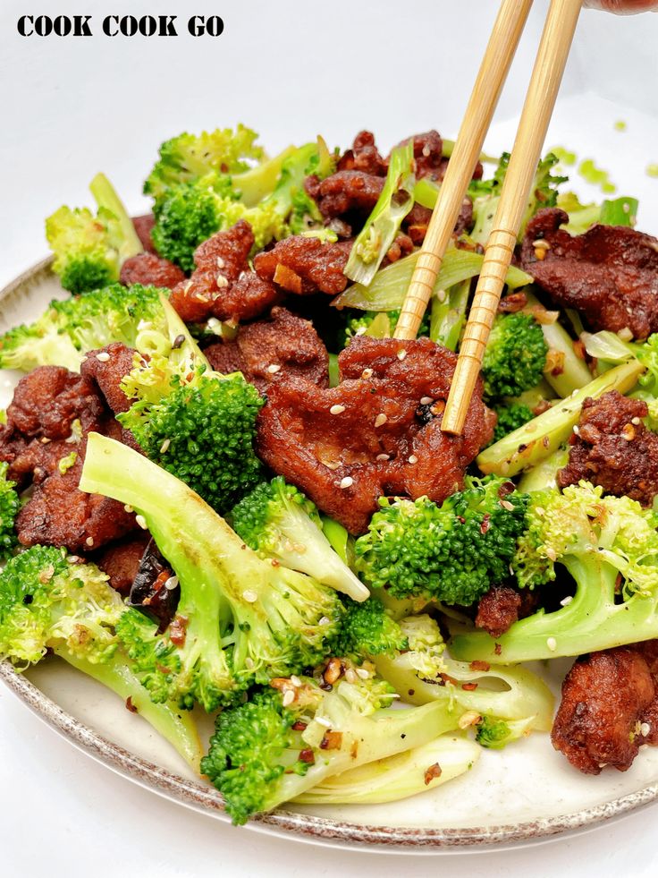 a plate filled with meat and broccoli topped with chopsticks