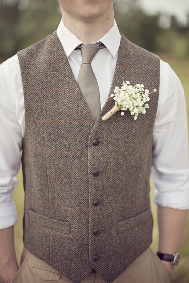 a man wearing a vest and tie with a flower on his lapel, standing in a field