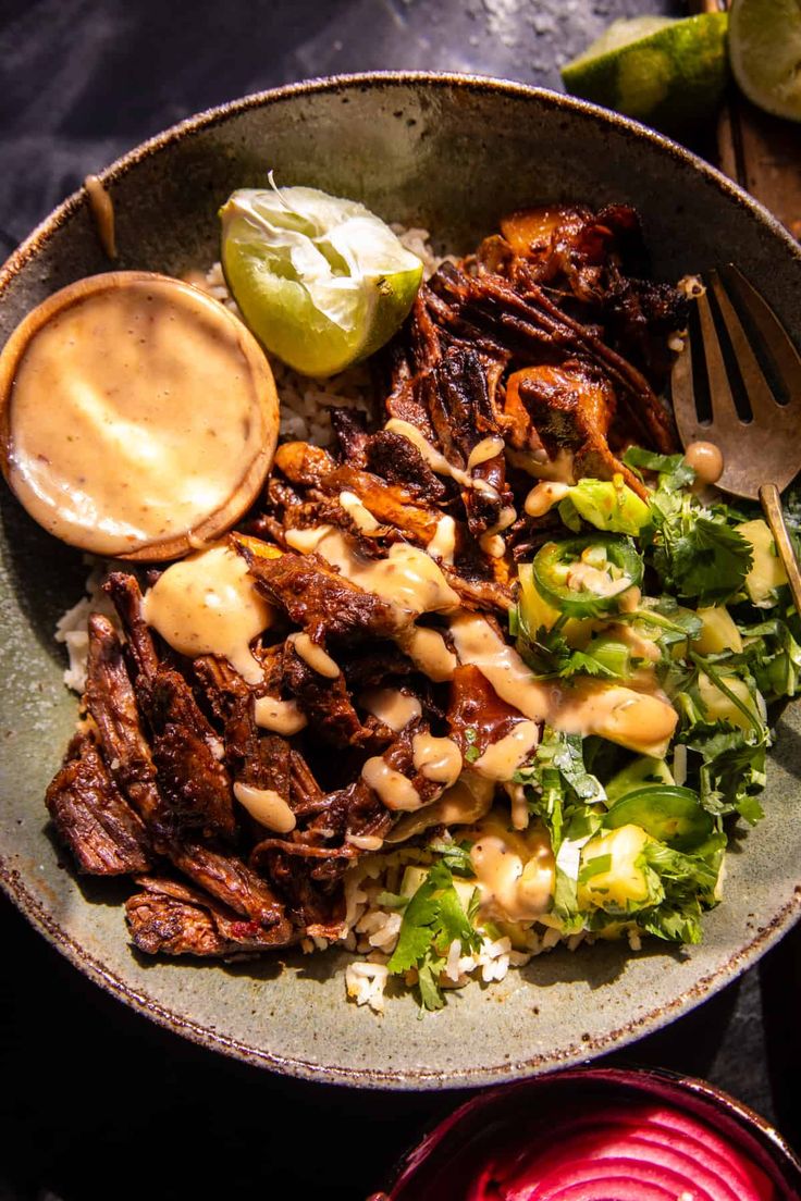 a bowl filled with meat and vegetables next to some sauce on top of the salad