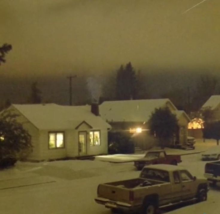 cars are parked in the snow on a residential street at night with houses and trees