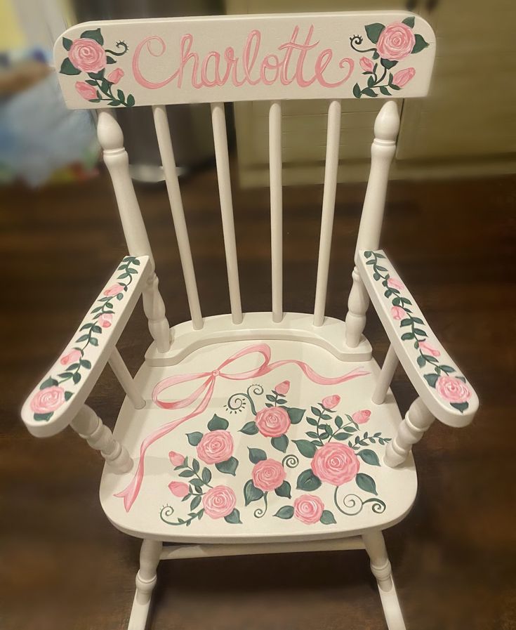 a white rocking chair with pink roses painted on the back and name charlotte written on it