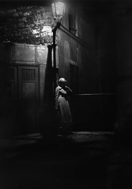 an old photo of a woman leaning against a pole in the dark with her head down