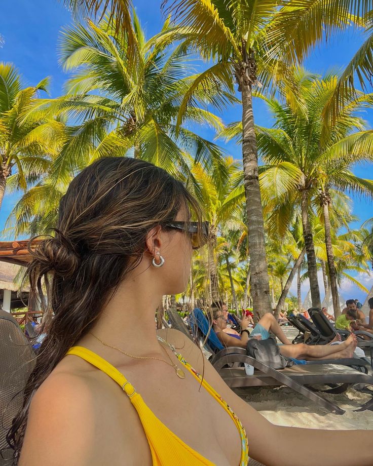 a woman in a yellow top is on the beach with palm trees and lounge chairs