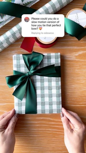 someone holding a wrapped present on top of a wooden table next to wrapping paper and ribbons