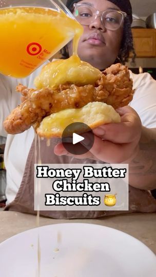 a woman holding up a chicken biscuit next to a glass of orange juice