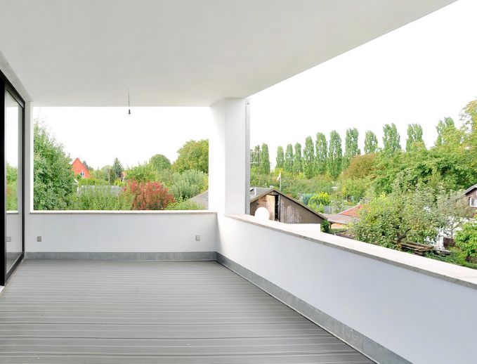 an empty balcony with wooden floors and white walls, overlooking the trees in the distance