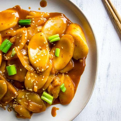 a white plate topped with meat covered in gravy and green onions next to chopsticks