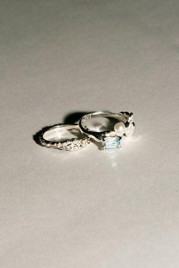 two silver rings with pearls on them sitting on a white surface, next to each other