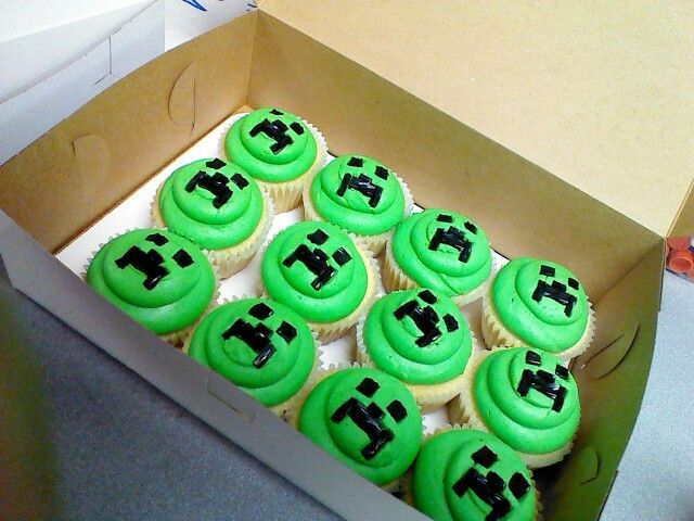 a box filled with green cupcakes covered in frosting and black icing