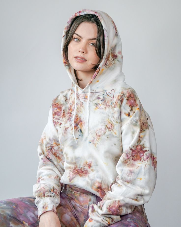 a woman sitting on top of a stool wearing a white hoodie and floral pants