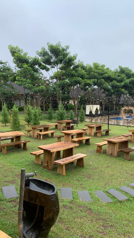 an empty picnic area with benches and trash can in the grass near a swimming pool