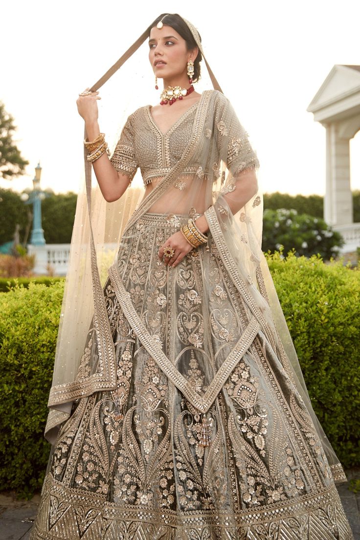 Description:- Embark on a new journey with our velvet bridal lehenga set featuring a sophisticated grey palette. Blending cultural crafts and a new-age spirit, the half-sleeved blouse with a V-neck, and lehenga feature zari & sequin embroidery. Crystal drops and heavy cheetha & zari work adorn the two net dupattas, making your dream wedding look come alive Style Tip: A semi-precious centre stone choker set and polki stone jadau bangles. Color Grey Fabric Velvet Occasion Party Wear Wedding Wear S Traditional Gray Lehenga For Festive Occasions, Gray Anarkali Set With Dupatta, Traditional Gray Festive Lehenga, Festive Gray Lehenga, Traditional Gray Festive Sets, Gray Wedding Sets For Eid, Festive Gray Lehenga With Zari Work, Gray Diwali Sets With Dupatta, Gray Sets With Dupatta For Diwali