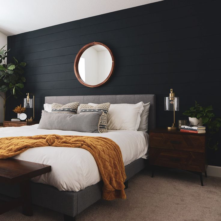 a bedroom with black walls and white bedding, wooden nightstands and round mirror on the wall