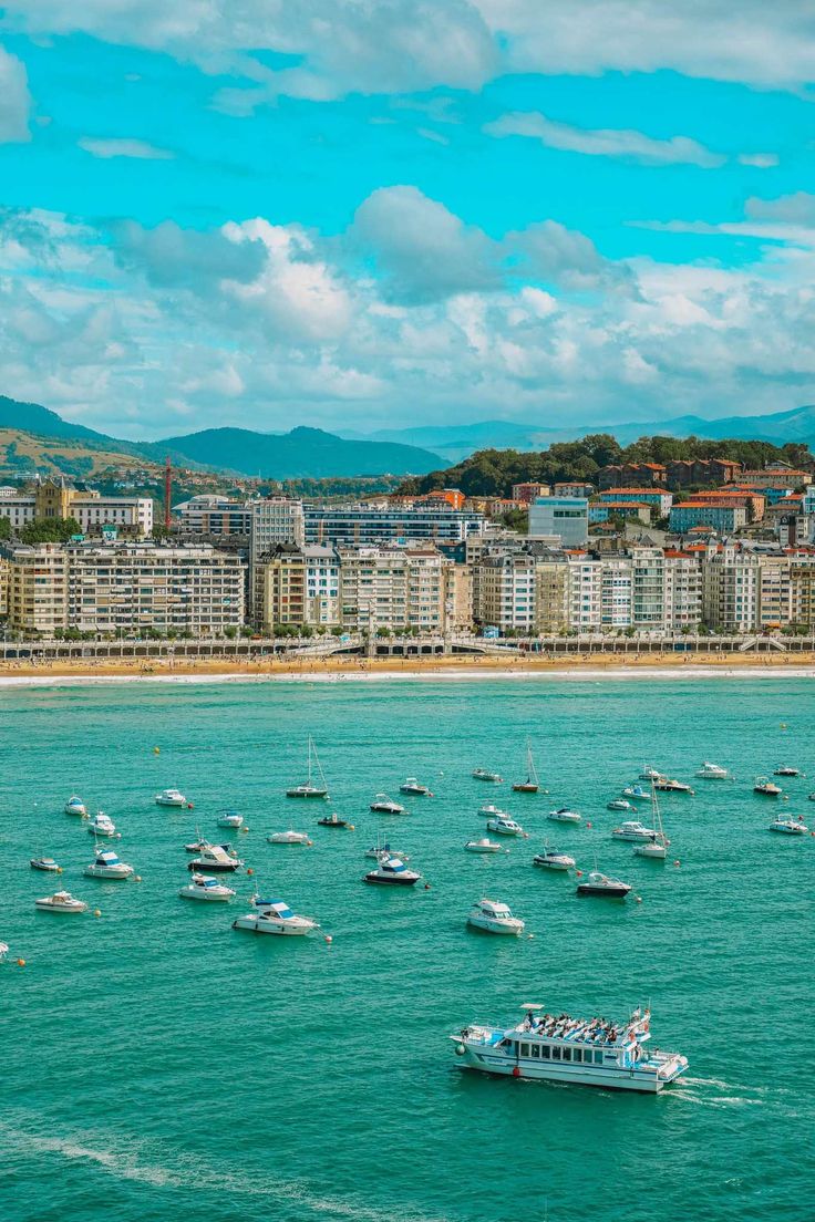 many boats are in the water near some buildings and hills with blue sky behind them