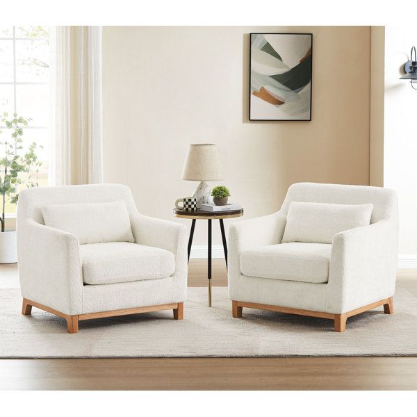 two white chairs sitting on top of a rug next to a table with a lamp