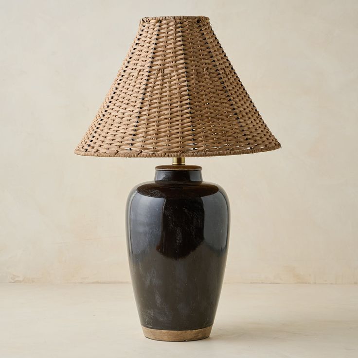 a table lamp with a brown base and a wicker shade on the top, against a beige background