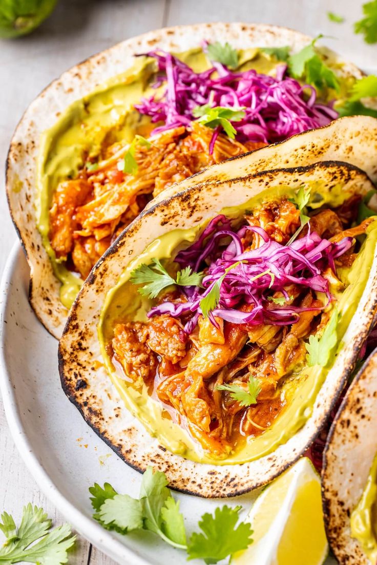 three tacos filled with meat, cole slaw and cilantro on a white plate