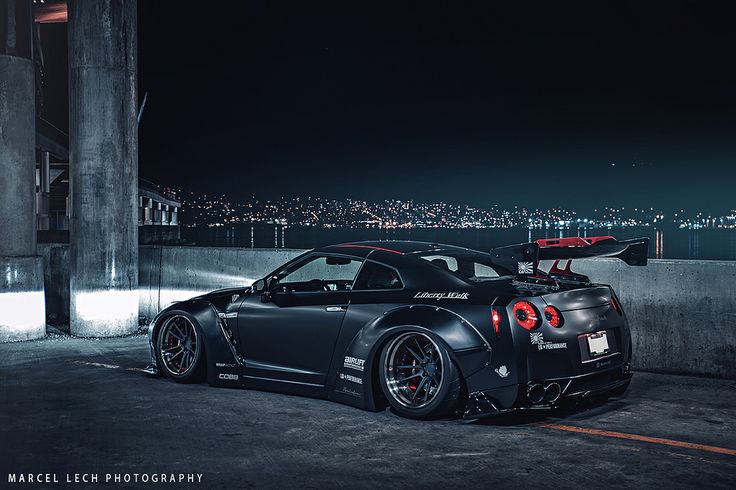 a black sports car parked in front of a building at night with the city lights behind it