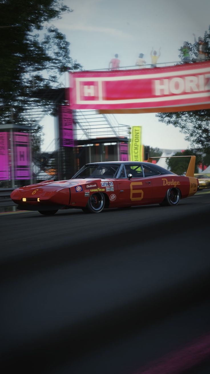 a red car driving down a street next to a gas station with a sign above it