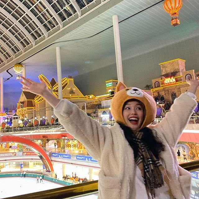 a woman wearing a cat hat and scarf standing in front of an indoor skating rink