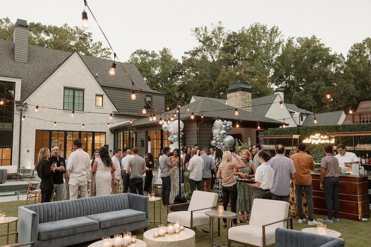 a group of people standing around in front of a house with outdoor seating and lights