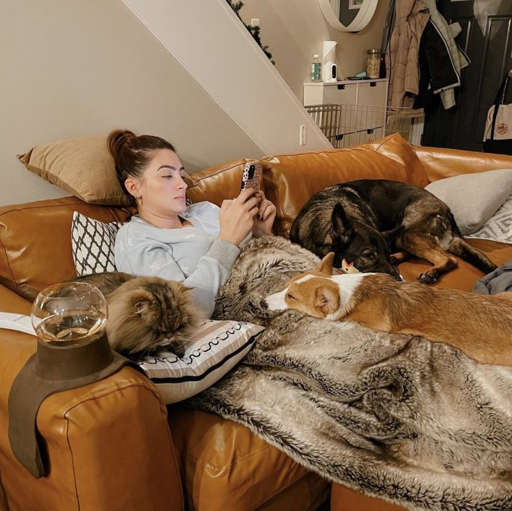 a woman sitting on a couch with two cats and dogs laying next to each other